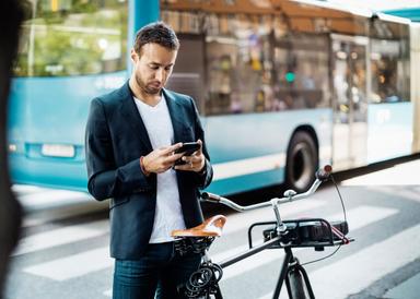 En man med cykel tittar i sin mobiltelefon, ståendes framför en buss.