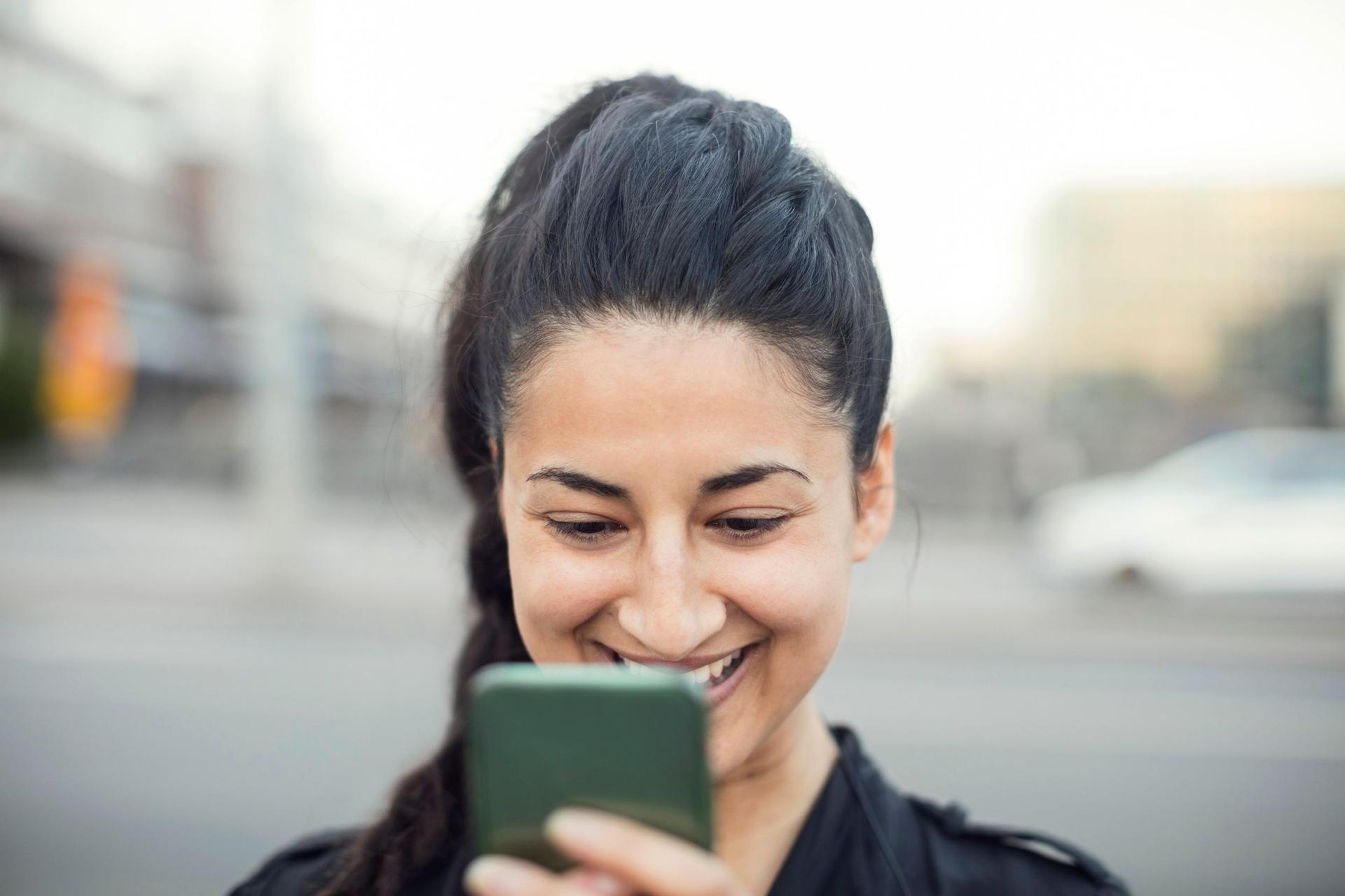 En ung kvinna tittar i sin mobiltelefon utomhus i en stad.