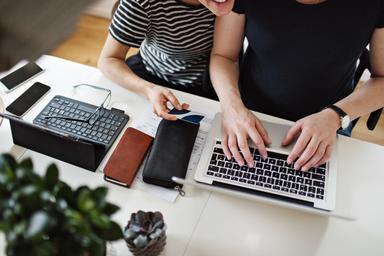 En kvinna och en man sitter och arbetar tillsammans på en laptop.